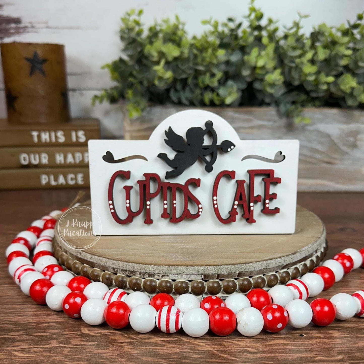 May include: A white wooden sign with a red and white "Cupid's Cafe" sign. A black silhouette of Cupid with an arrow is above the text.